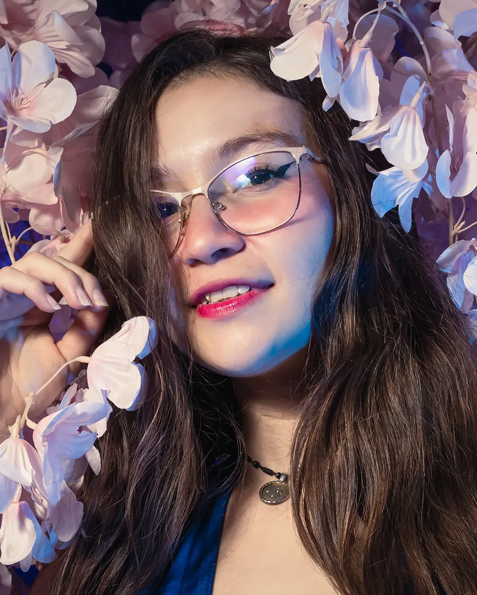 Modelo sonriente con gafas entre flores lila, luz violeta del studio
